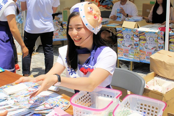 なぜか「ひょっとこ」のお面を装着して来場者にうちわを配る横浜開港祭親善大使の持田凪沙さん（臨港パーク）