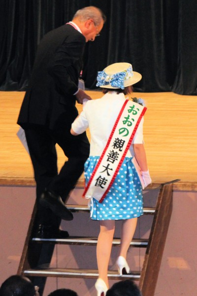 壇上に上がる大野町（岐阜県）の宇佐美晃三町長を支援する「おおの親善大使」河村梨花さん（長井市民文化会館）